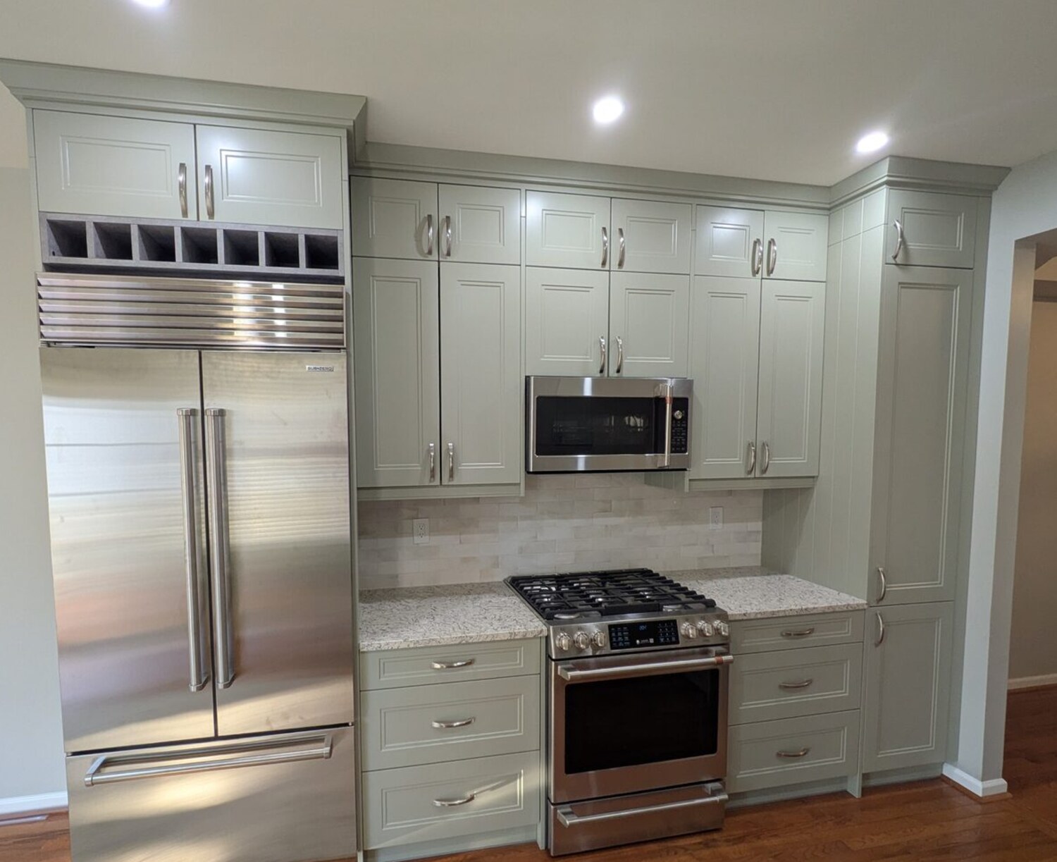 Sage-green kitchen with built-in wine storage, pro-style stainless refrigerator, granite counters and oak floors