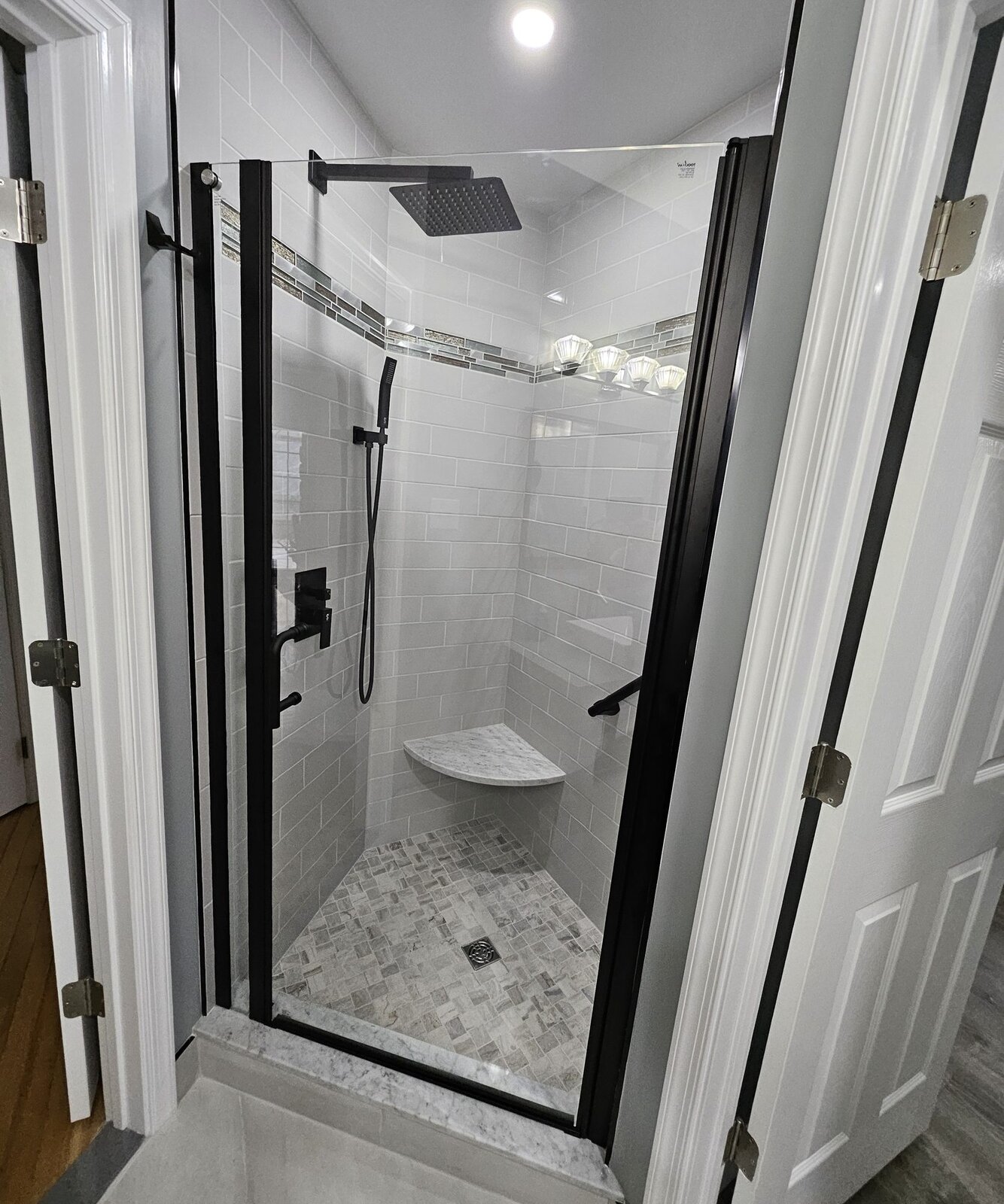 Black-framed glass shower with marble tile and mosaic floor