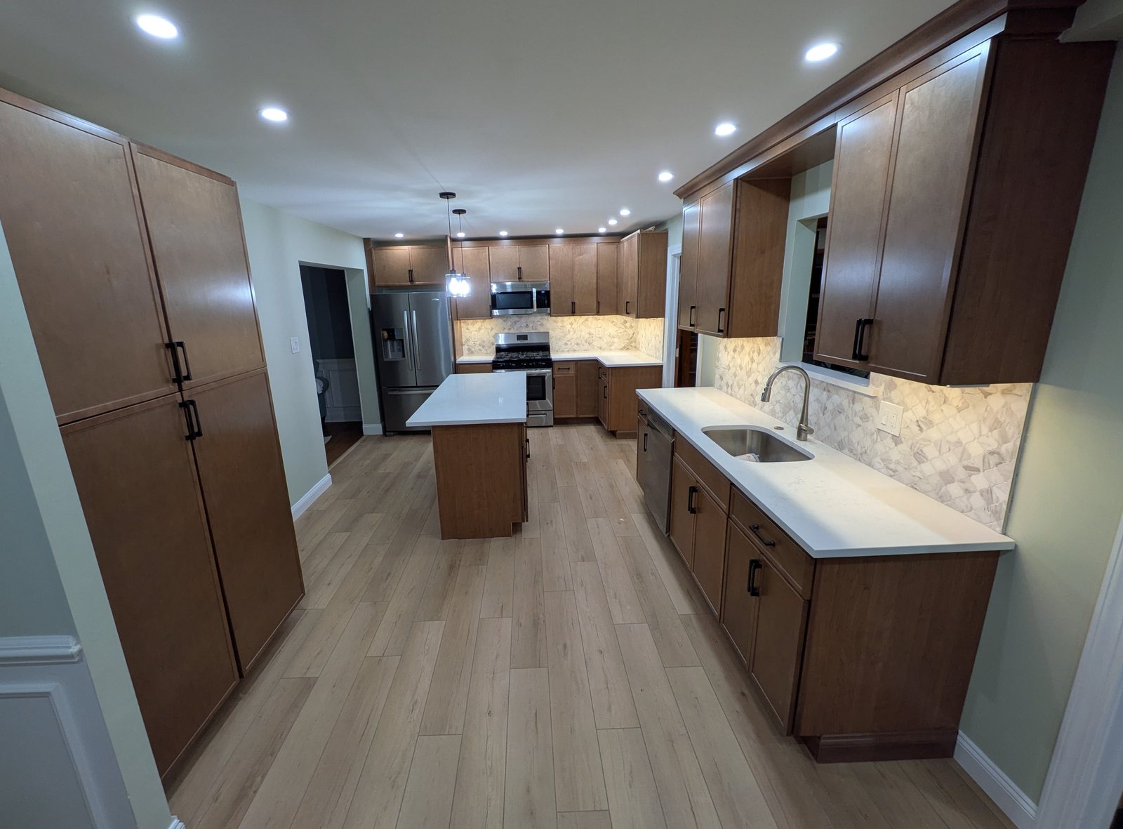 Opened kitchen in Horsham, PA with hazelnut shaker cabinets, a white quartz island, pantry cabinets and recessed lights